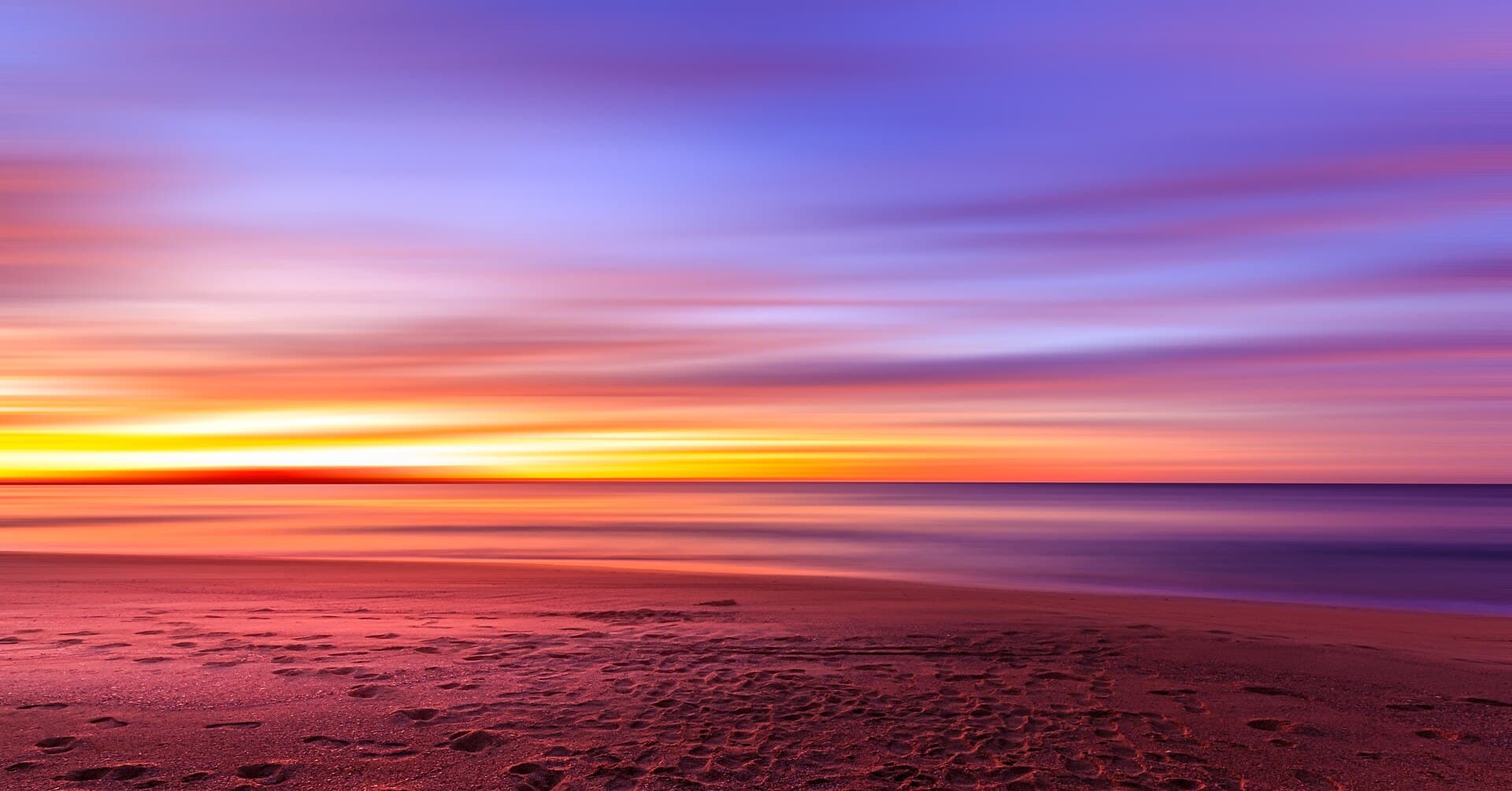 Long-exposure sunset over a New South Wales beach, the water a deep violet and the sky fading from gold to indigo.